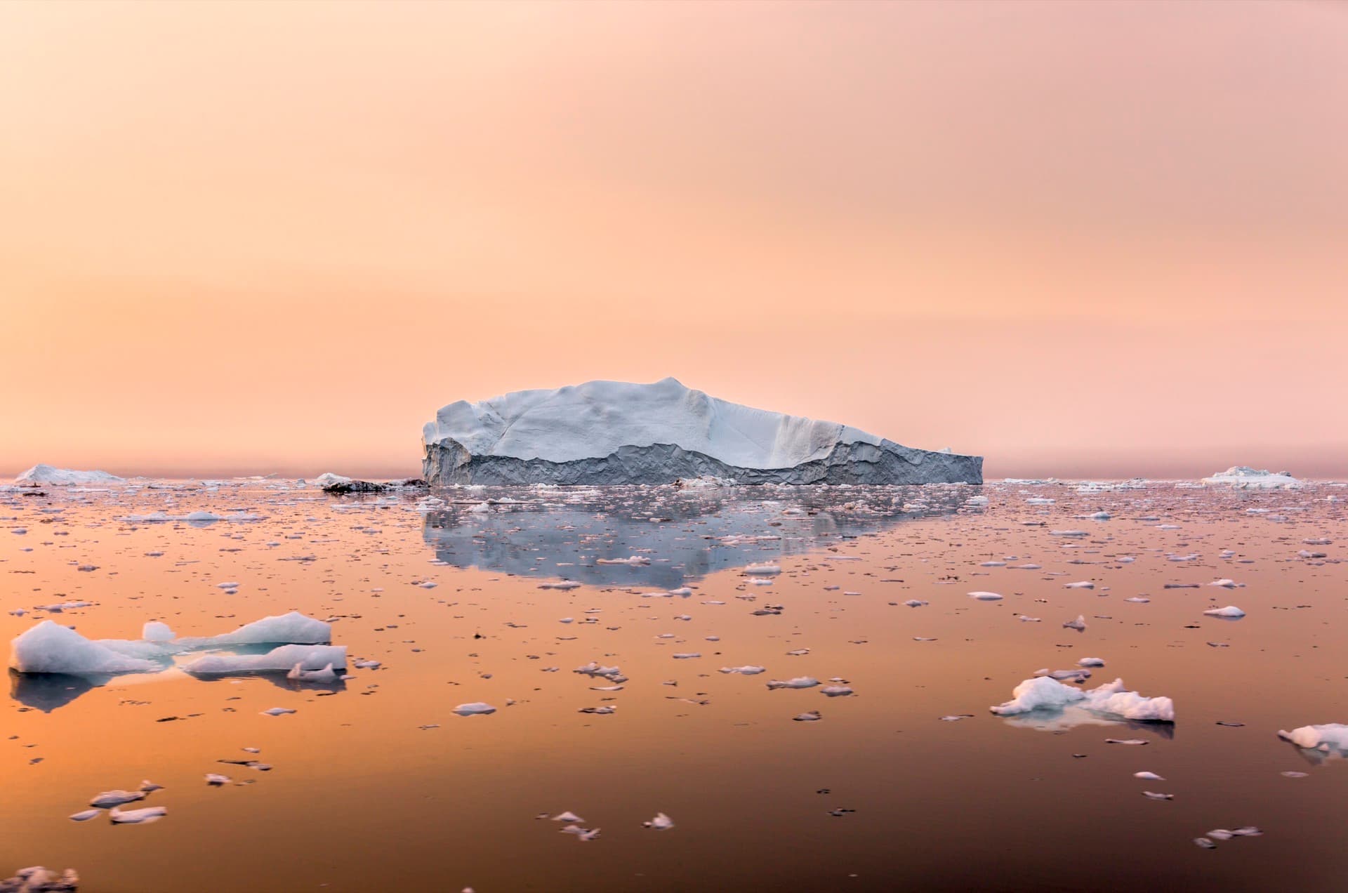 Iceberg reflected in still Arctic water at sunset